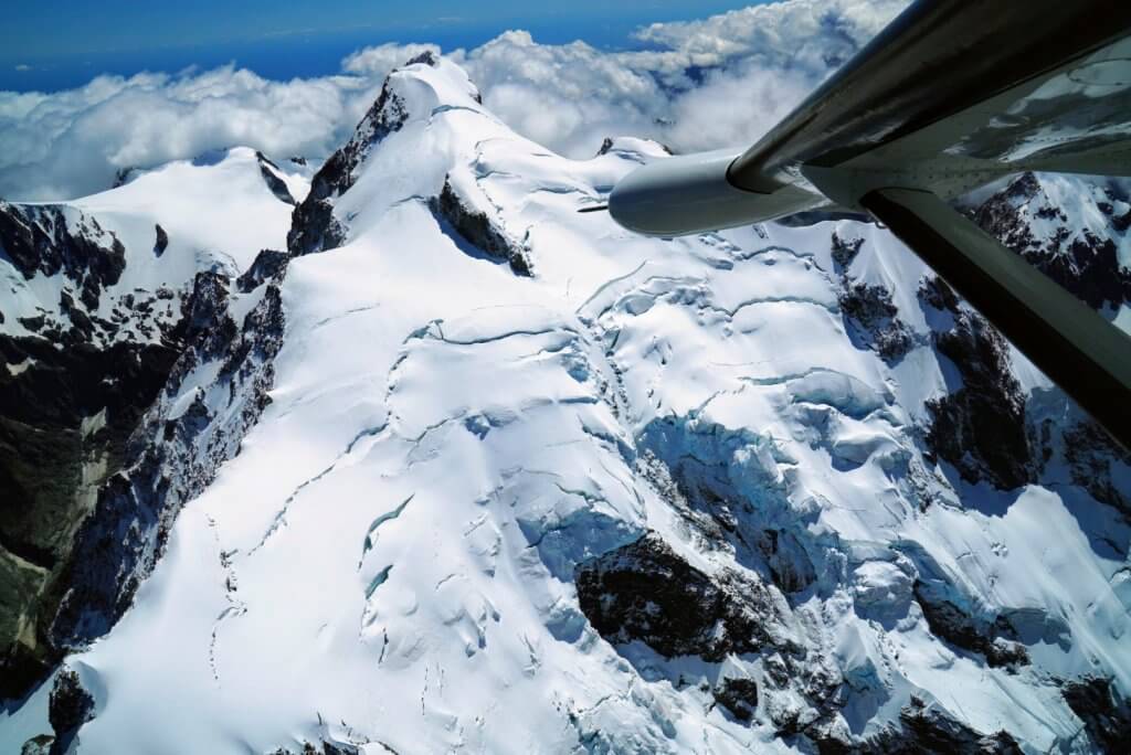 A small plane flying over snowy mountains in New Zealand