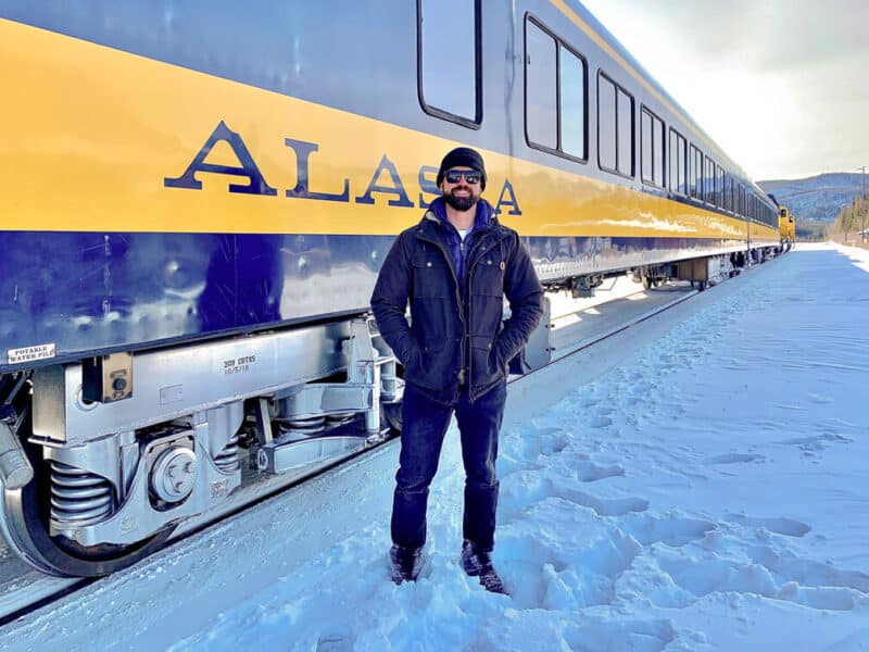 A man stands in front of the Alaskan Aurora Winter Train