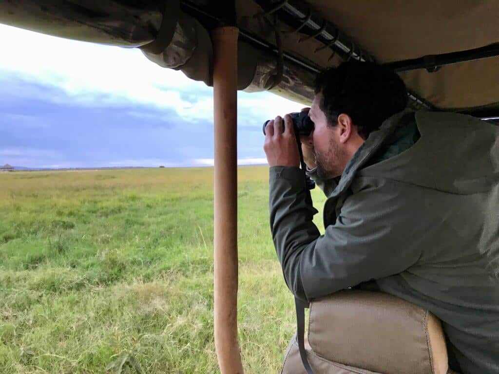 A man looks through binoculars out onto the African planes