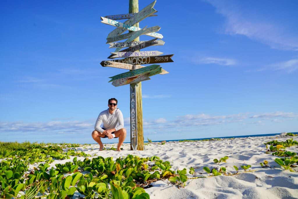 man on beach in turks and caicos near paradise sign
