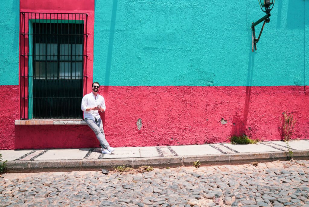 Man sits on windowsill outside of brightly colored blue and red Mexican building