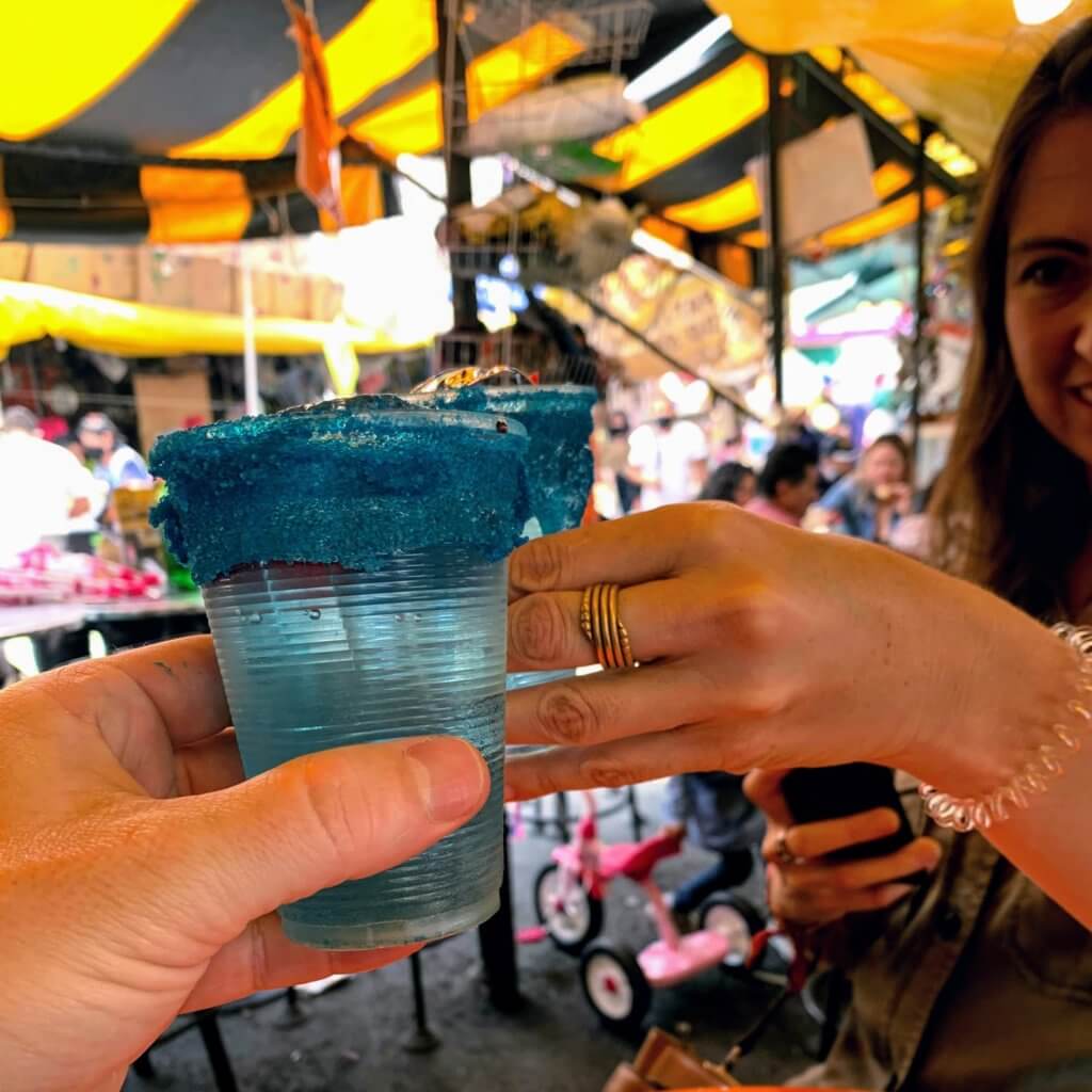 two people holding up their blue cocktails in a mexico city market
