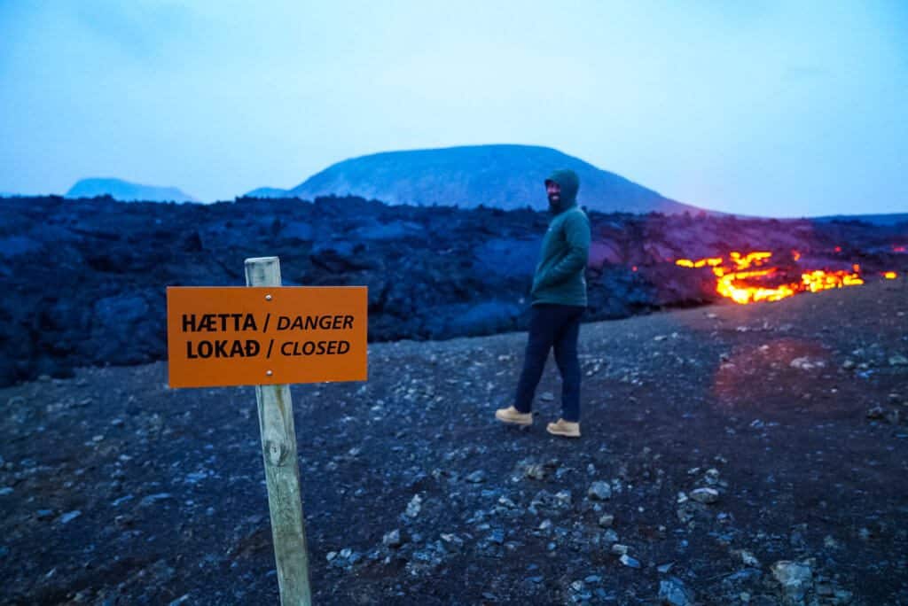 man walks past danger sign near flowing lava 