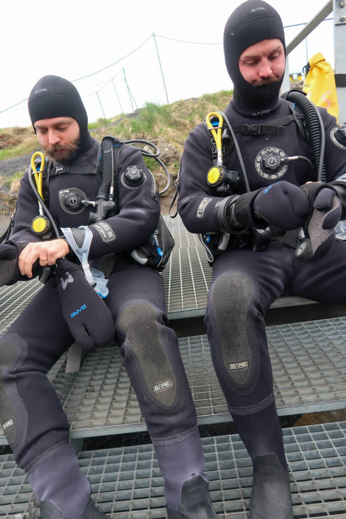 two mean put on drysuits to scuba dive in inceland